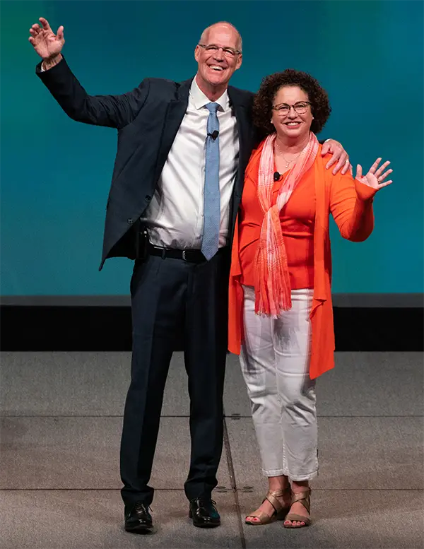 Bob and Susan Negen on stage at the Retail Success Summit, arms raised in welcome